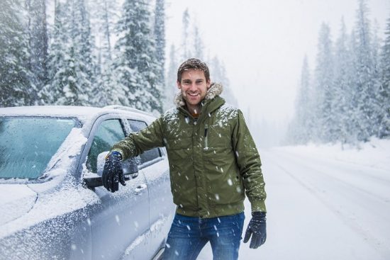 Caucasian man leaning on car in snow